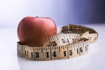 Photo for Red apple wrapped in a tape measure isolated on a violet background - Royalty Free Image