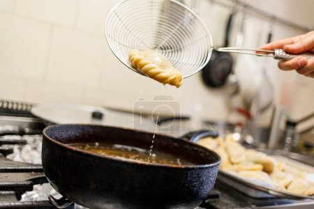 Téléchargez les photos : Détail de la préparation de raviolis frits dans une casserole pleine d'huile dans une cuisine traditionnelle - en image libre de droit