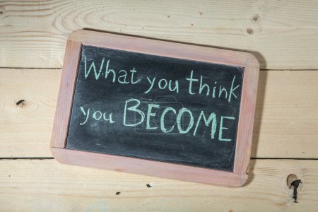 Téléchargez les photos : Tableau noir sur fond en bois avec l'inscription : "Ce que tu penses devenir" - en image libre de droit