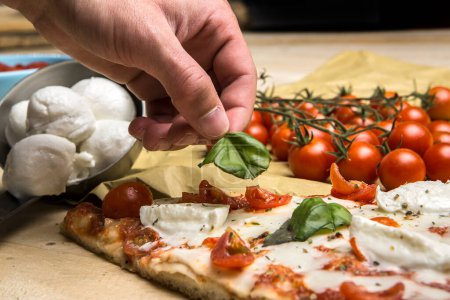 Photo for A person's hand takes a slice of tomato pizza over a wooden table - Royalty Free Image