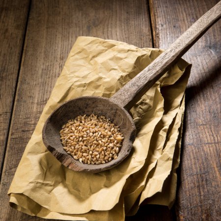 Photo for Wheat on antique ladle on paper isolated on wooden table - Royalty Free Image