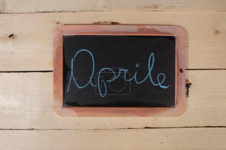 Photo for Blackboard with the inscription 'April' on a wooden background - Royalty Free Image
