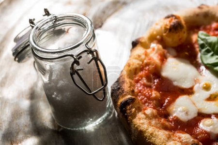 Téléchargez les photos : Petit récipient en verre pour sel grossier à côté d'une pizza margherita - en image libre de droit
