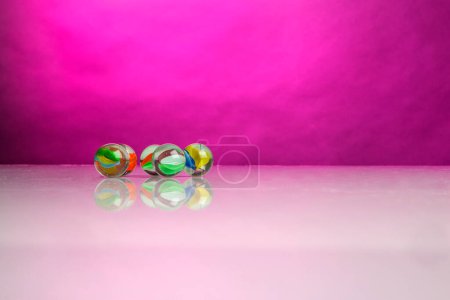 Téléchargez les photos : Marbres en verre coloré sur une surface réfléchissante avec un fond fuchsia - en image libre de droit