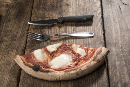 Foto de Rebanada de pizza con cuchillo y tenedor descansando sobre mesa de madera - Imagen libre de derechos