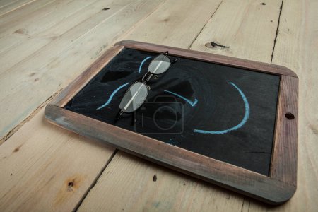 Téléchargez les photos : Tableau noir avec un visage et de vraies lunettes dessinées, isolées sur une table en bois - en image libre de droit