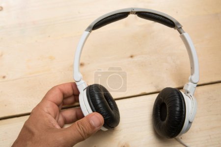 Téléchargez les photos : Écouteurs modernes blancs tenus par une main sur une table en bois - en image libre de droit