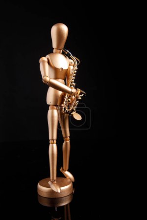 Téléchargez les photos : Cagliari, Italie - 12 janvier 2011 : Marionnette en bois joue un saxophone doré, isolé sur fond noir - en image libre de droit