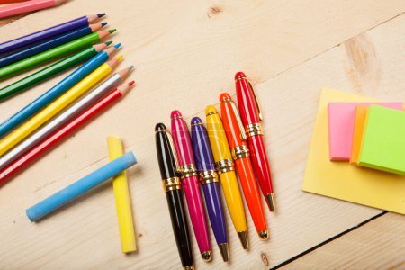 Photo for Pencils, pens, chalks and post-it notes on wooden tabletop - Royalty Free Image