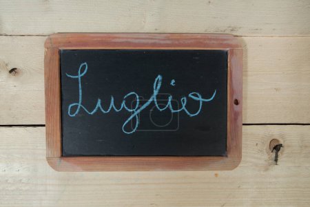 Photo for Chalkboard with 'July' lettering on wooden background - Royalty Free Image