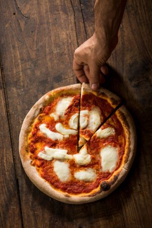 Foto de Pizza margherita cortada con una cuña disparada desde arriba aislada sobre una mesa de madera - Imagen libre de derechos