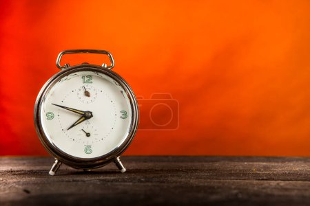 Foto de Reloj redondo vintage sobre mesa de madera y fondo naranja - Imagen libre de derechos