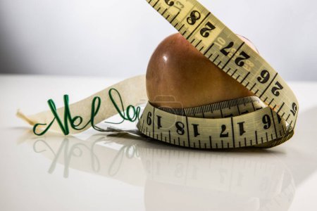 Photo for Measuring tape around an apple with green lettering detail. - Royalty Free Image