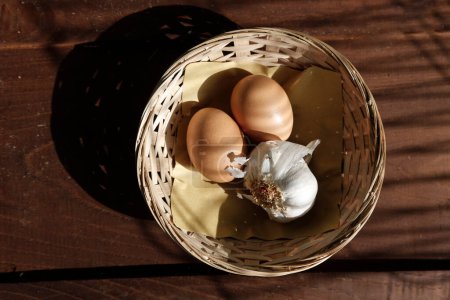 Téléchargez les photos : Œufs et ail dans un panier en osier sur une table - en image libre de droit