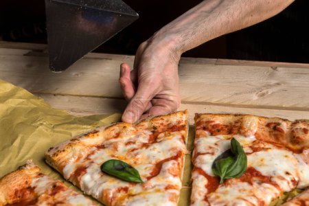 Foto de La mano de una persona toma una rebanada de pizza de tomate sobre una mesa de madera - Imagen libre de derechos