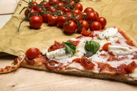 Téléchargez les photos : Détail d'un coin de pizza avec tomate et mozzarella sur une table en bois - en image libre de droit