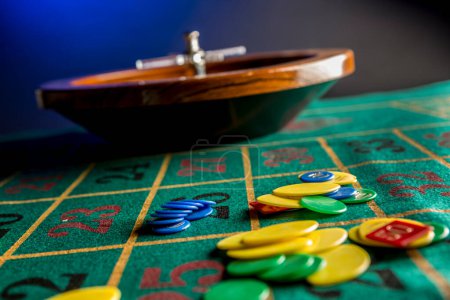 Téléchargez les photos : Roulette in legno isolata sopra un tavolo da gioco verde con fiches colorate - en image libre de droit