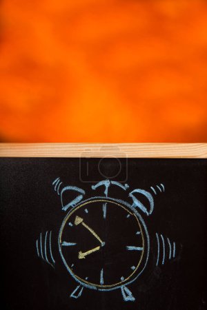 Foto de Despertador dibujado en tiza sobre una pizarra aislada sobre fondo naranja - Imagen libre de derechos