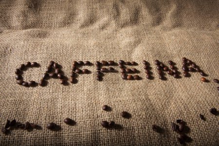 Foto de Escrito "cafeína" con granos de café sobre un saco de yute - Imagen libre de derechos