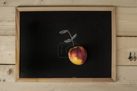 Photo for Blackboard with a peach on it and perspective drawing of peach leaves, isolated on a wooden table - Royalty Free Image