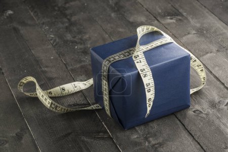 Photo for Blue gift box with dressmaker tape around on wooden table background - Royalty Free Image