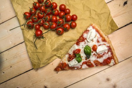 Foto de Detalle de una cuña de pizza con tomate y mozzarella sobre una mesa de madera - Imagen libre de derechos
