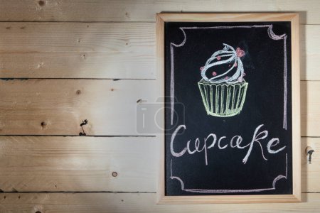 Photo for Black chalkboard on wooden background with the inscription: "Cupcake" and the drawing of a cake - Royalty Free Image