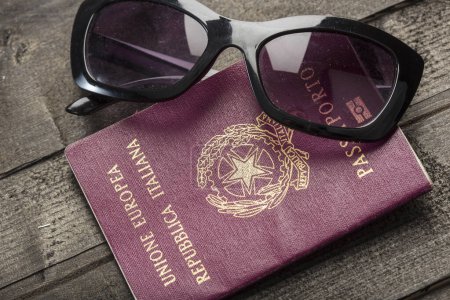 Téléchargez les photos : Passeport italien placé sur une table à côté d'autres objets avec une carte géographique - en image libre de droit