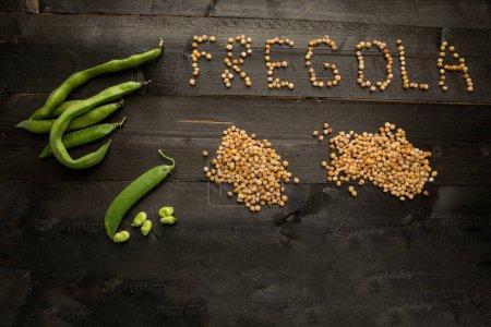 Téléchargez les photos : Lettrage "Fregola" avec des grains de pâtes en vrac, isolé sur une table en bois sombre - en image libre de droit