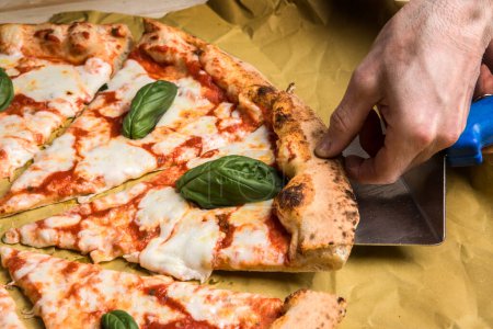 Téléchargez les photos : La main d'une personne prend une tranche de pizza tomate sur une table en bois - en image libre de droit
