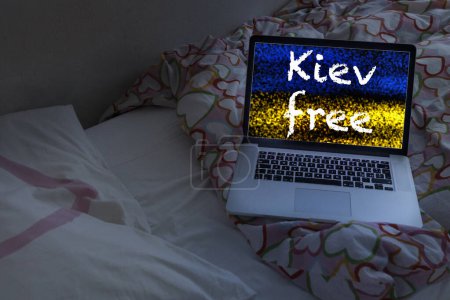 Téléchargez les photos : Ordinateur portable sur le lit avec le texte "Kiev gratuit" et drapeau ukrainien - en image libre de droit