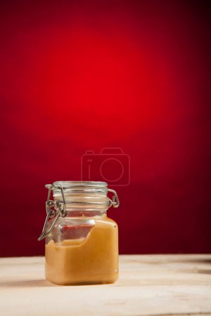Foto de Tarro de vidrio con crema sobre mesa de madera aislada sobre fondo rojo - Imagen libre de derechos