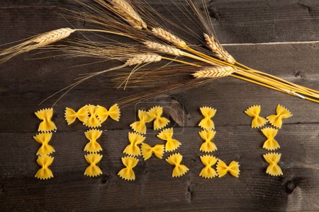 Photo for Composition with short pasta and ears of wheat on a dark table to form the word "Italy" - Royalty Free Image