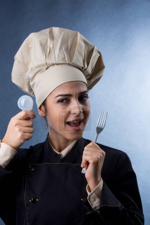 Photo for Chef woman in chef uniform holds a light bulb in her hand to signify the search for a good idea for a creative recipe, isolated on light background - Royalty Free Image