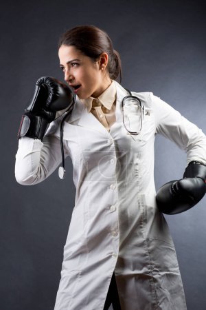 Photo for Female doctor in white coat and boxing gloves and ready for confrontation and battle, isolated on white background - Royalty Free Image