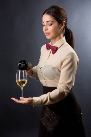 Photo for Beautiful and elegant waitress with shirt and red bow tie is ready to offer a glass of wine, isolated on a black background - Royalty Free Image
