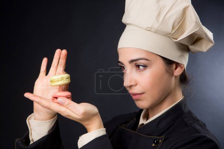 Photo for Chef woman holds colorful macarons in hand checking the size and composition, isolated on black background - Royalty Free Image