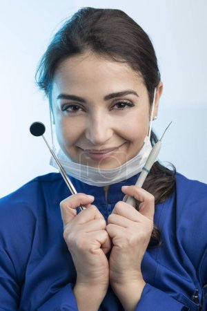 Photo for Female dentist in a surgical mask and blue coat shows the work tools, isolated on a white background - Royalty Free Image