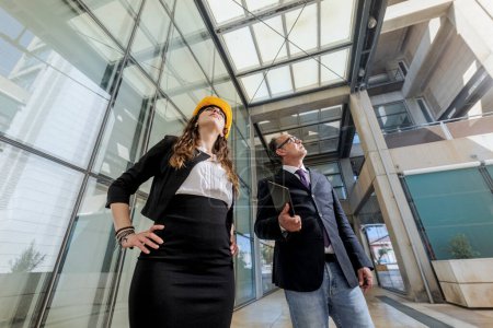 Photo for Couple of engineers with protective helmets on their heads check the state of a modern construction by discussing with each other - Royalty Free Image