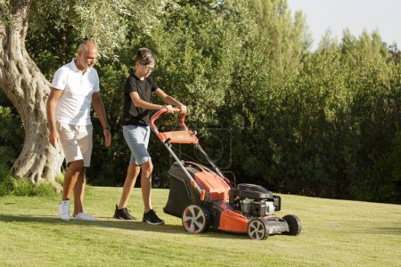 Photo for Dad with son cut the grass with the lawn mower in the home garden - Royalty Free Image