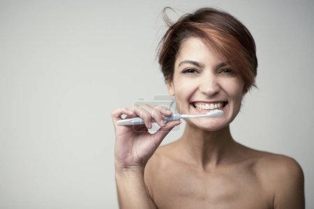 Photo for Beautiful girl with short hair brushes her teeth with a toothbrush, isolated on light background - Royalty Free Image