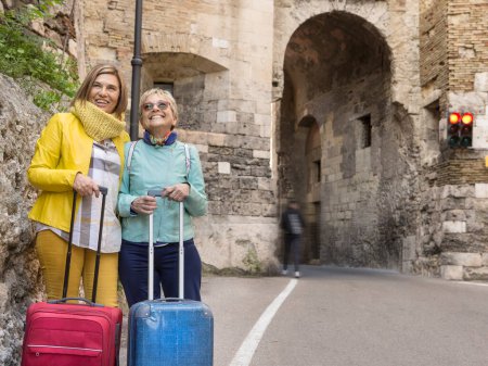 Photo for Elderly tourists with hats and colored clothes having fun around the city with their suitcases - Royalty Free Image