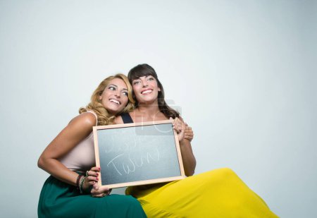 Téléchargez les photos : Jumeaux (une blonde et une brune) souriant tenant un tableau noir qui dit "amour Twin" - en image libre de droit