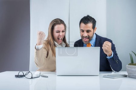 Foto de Un par de colegas de negocios están contentos con los resultados obtenidos sentados en la oficina frente al escritorio con un ordenador portátil. Aislado sobre un fondo negro. - Imagen libre de derechos