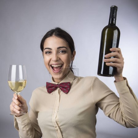 Photo for Black-haired waitress with shirt and red bow tie toasts happy with wine and a goblet, isolated on light background - Royalty Free Image