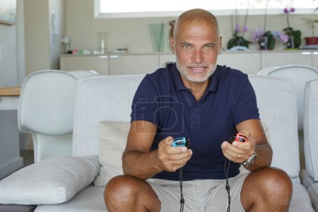 Téléchargez les photos : Un homme de cinquante ans joue à un jeu électronique dans son salon - en image libre de droit