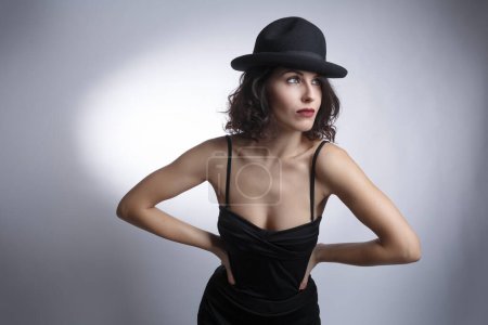 Téléchargez les photos : Belle brune dans une robe noire et chapeau noir posant isolé sur un fond blanc. - en image libre de droit