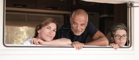 Téléchargez les photos : Heureuse famille souriante regardant par la fenêtre de leur camping-car - en image libre de droit