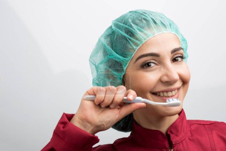 Téléchargez les photos : Dentiste avec capuchon vert sur la tête et manteau rouge est indécis entre la brosse à dents et le miroir dentaire - en image libre de droit