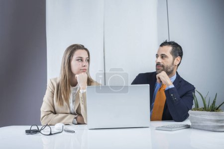 Photo for Pair of business colleagues are happy with the results achieved sitting in the office in front of the desk with a laptop. Isolated on a black background. - Royalty Free Image